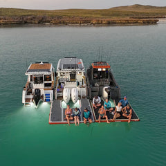 3 blue dog boats moored side by side with inflatable floatables pontoons docks and people sitting on the pontoons